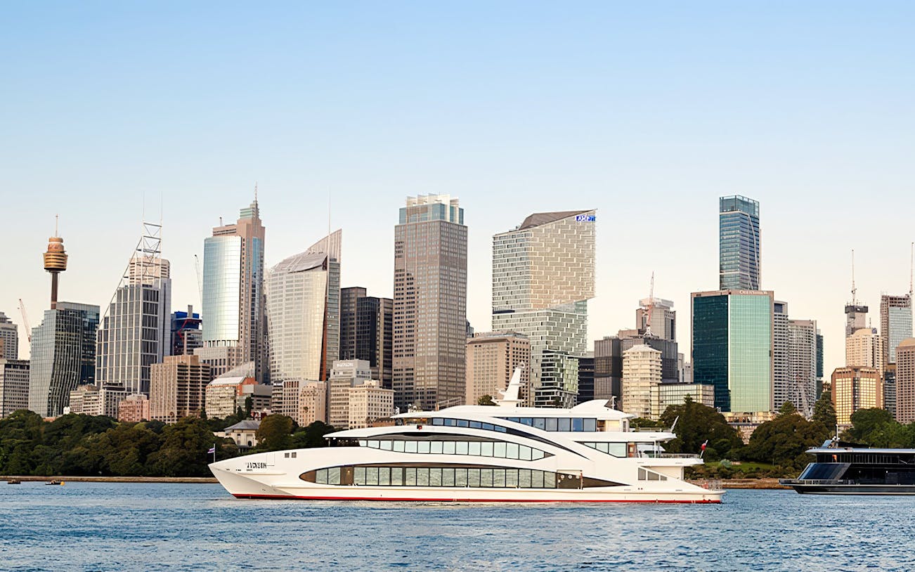 Luxury yacht The Jackson cruising in Sydney Harbour with city skyline backdrop.