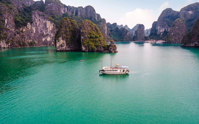 Cruise ship in Ha Long Bay's emerald waters, surrounded by limestone islands.
