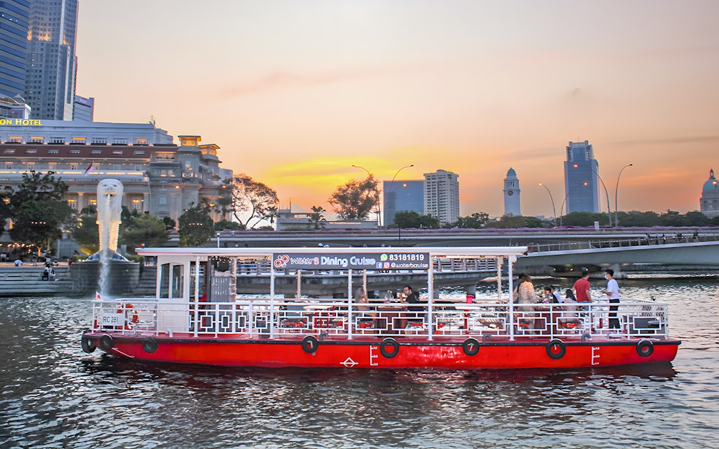Singapore River Cruise boat by WaterB passing Merlion Park at sunset.