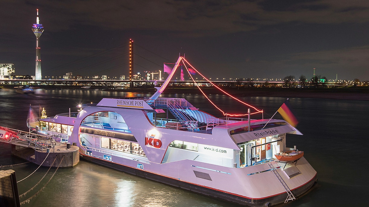 Cruise ship on the Rhine River at night with Düsseldorf skyline in the background.