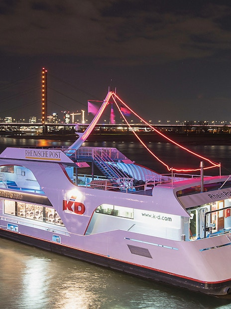 Cruise ship on the Rhine River at night with Düsseldorf skyline in the background.