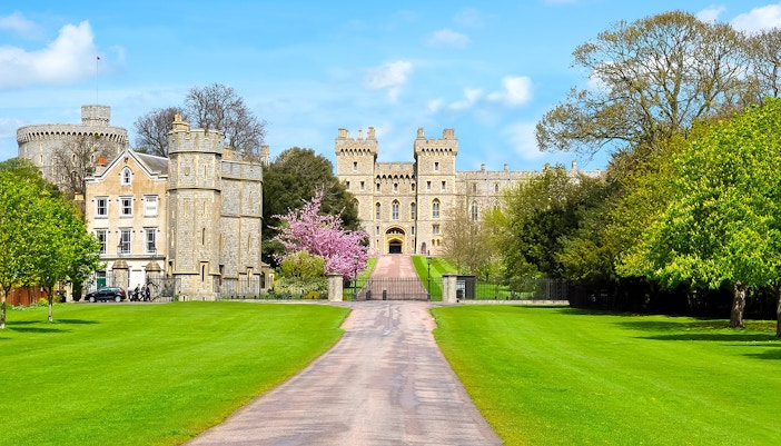 Windsor Castle exterior with stone towers and lush green gardens.