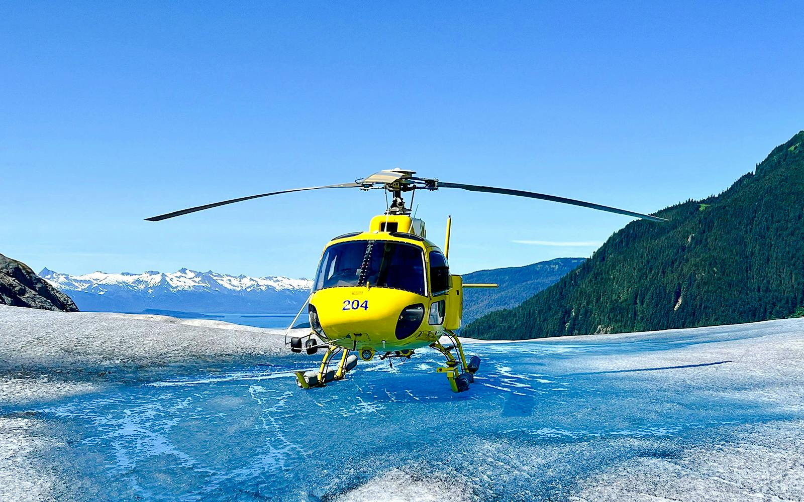 Yellow helicopter on glacier during Juneau tour with mountain backdrop.