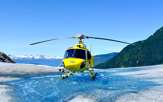 Yellow helicopter on glacier during Juneau tour with mountain backdrop.