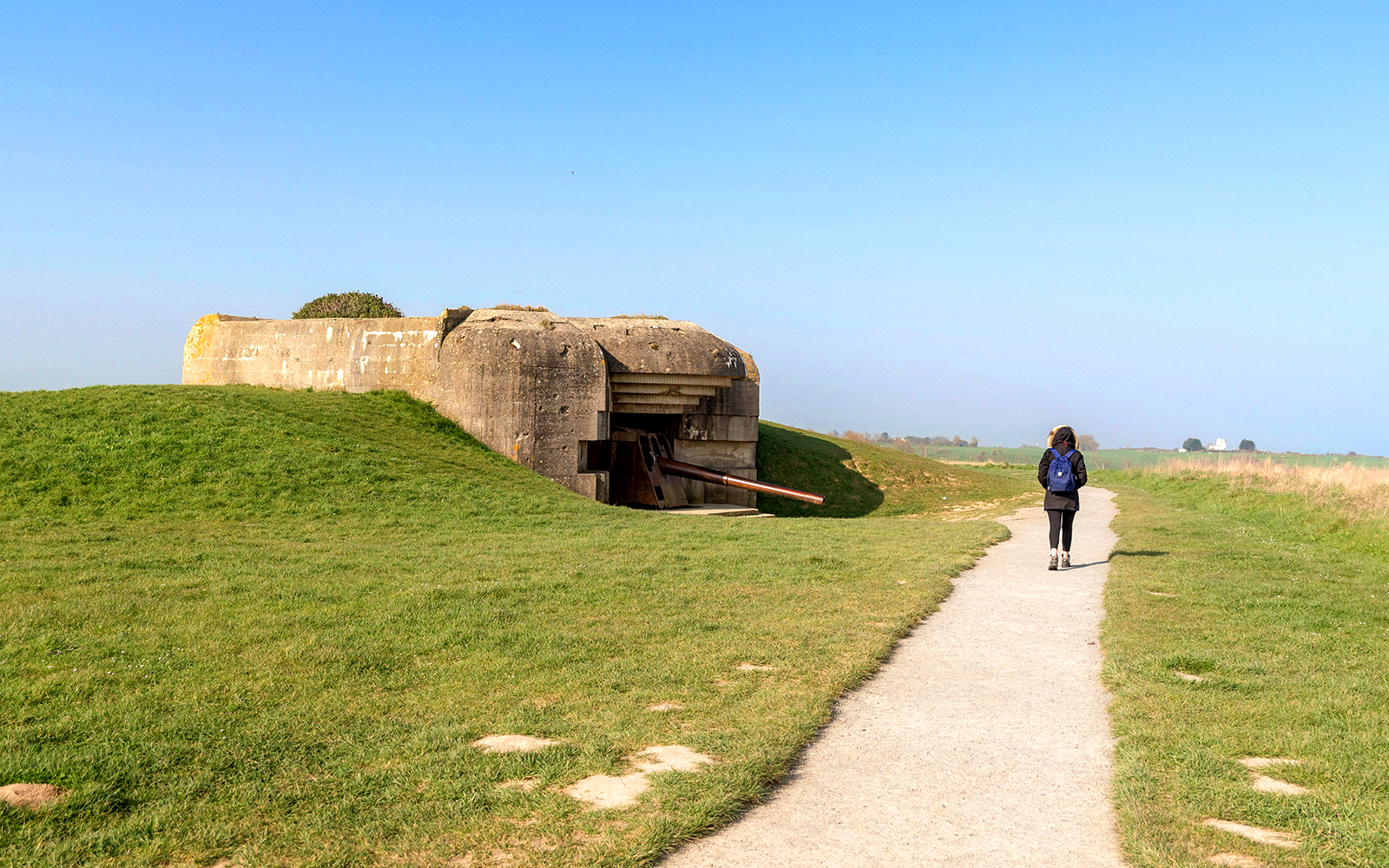 Path leading to a World War II bunker in Normandy, France, with a person walking.