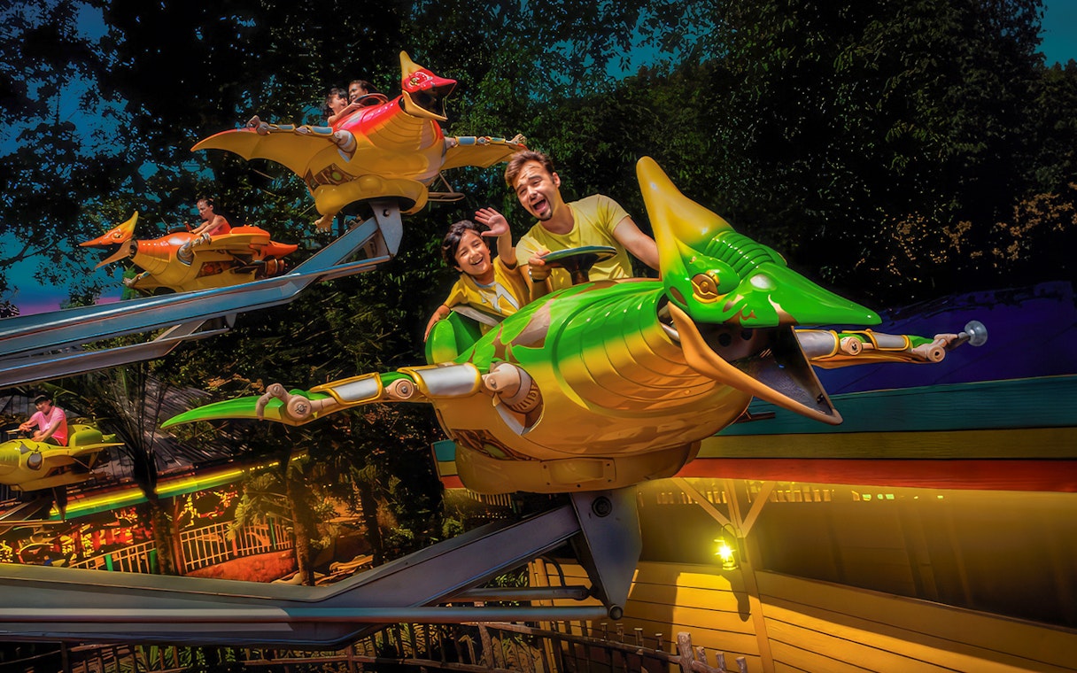 Father and son enjoying Flying Dinosaur ride at theme park.