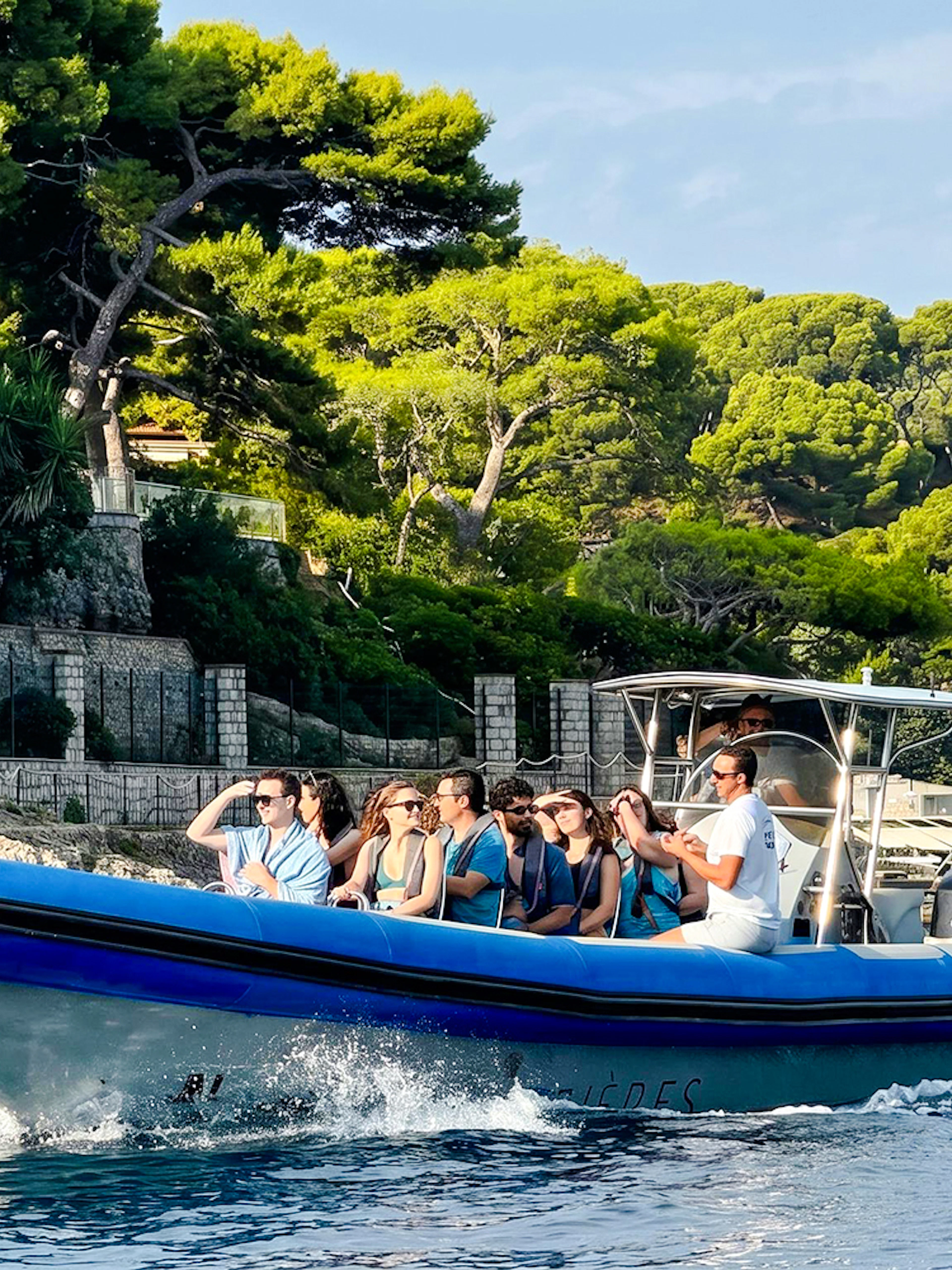 Boat tour group cruising near Villefranche coastline with lush greenery.