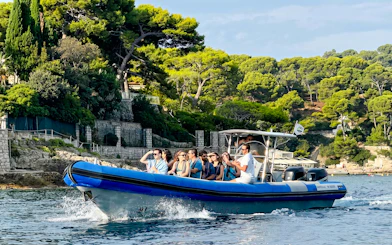 Boat tour group cruising near Villefranche coastline with lush greenery.