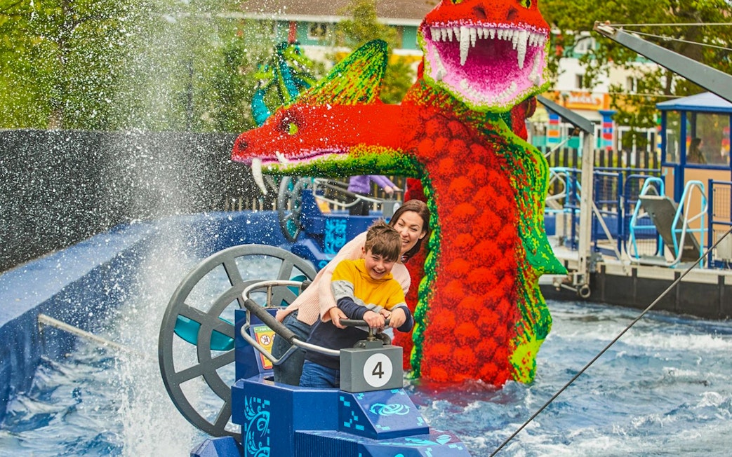 Child steering a boat near a LEGO dragon at LEGOLAND Windsor Resort.