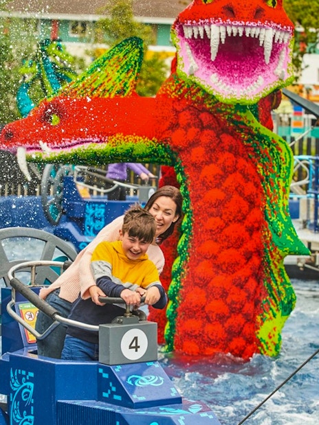Child steering a boat near a LEGO dragon at LEGOLAND Windsor Resort.