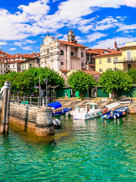 Hop-on hop-off boat docked at Isole Borromee with historic buildings in the background.