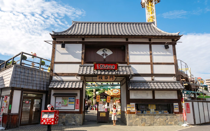 Traditional entrance gate of Asakusa Hanayashiki amusement park with visitor under blue sky.