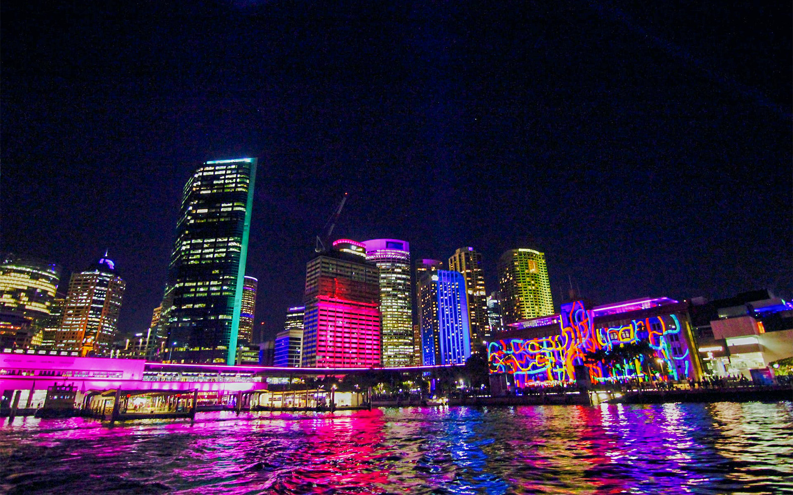 Lit up buildings in Sydney Harbour during Vivid Sydney Cruise.