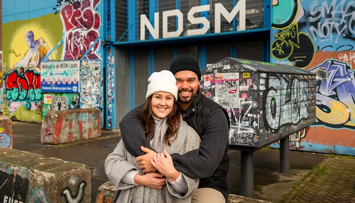 Couple posing at NDSM Amsterdam with vibrant graffiti backdrop.
