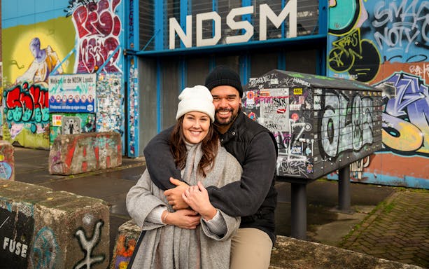 Couple posing at NDSM Amsterdam with vibrant graffiti backdrop.