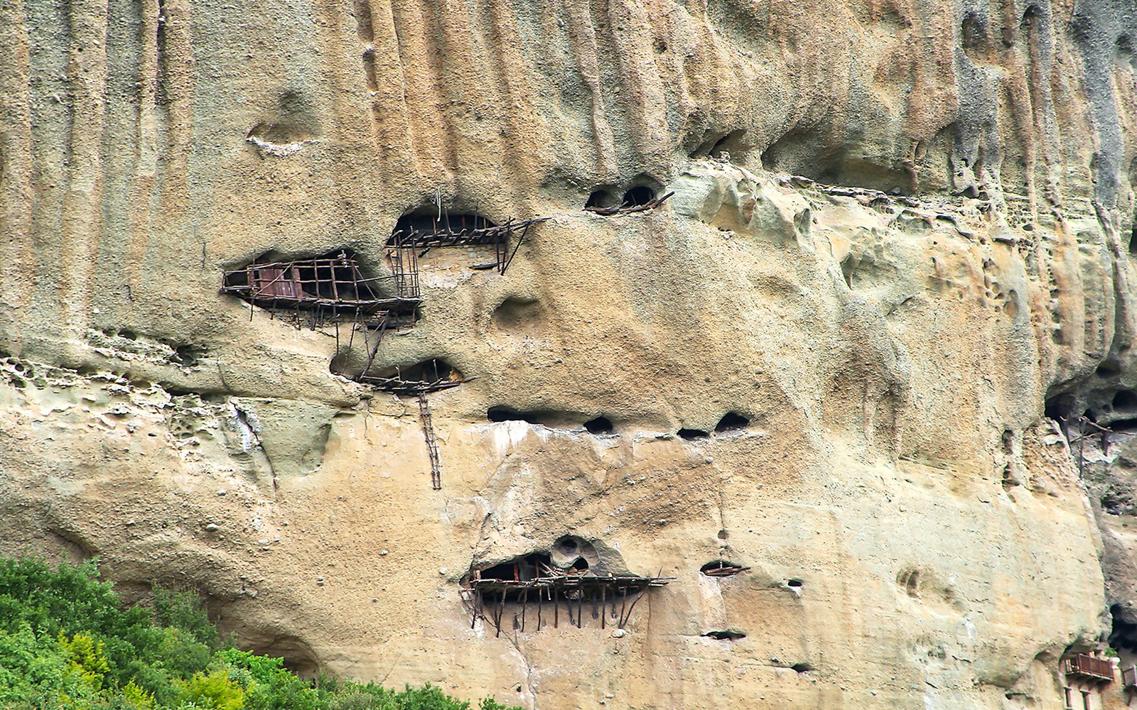 Ancient Meteora cliffside caves with wooden structures in Greece.