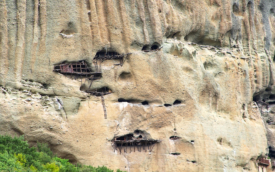 Ancient Meteora cliffside caves with wooden structures in Greece.