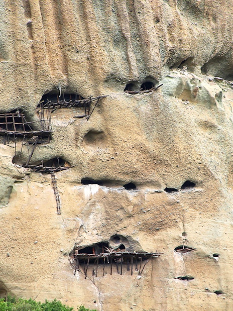 Ancient Meteora cliffside caves with wooden structures in Greece.