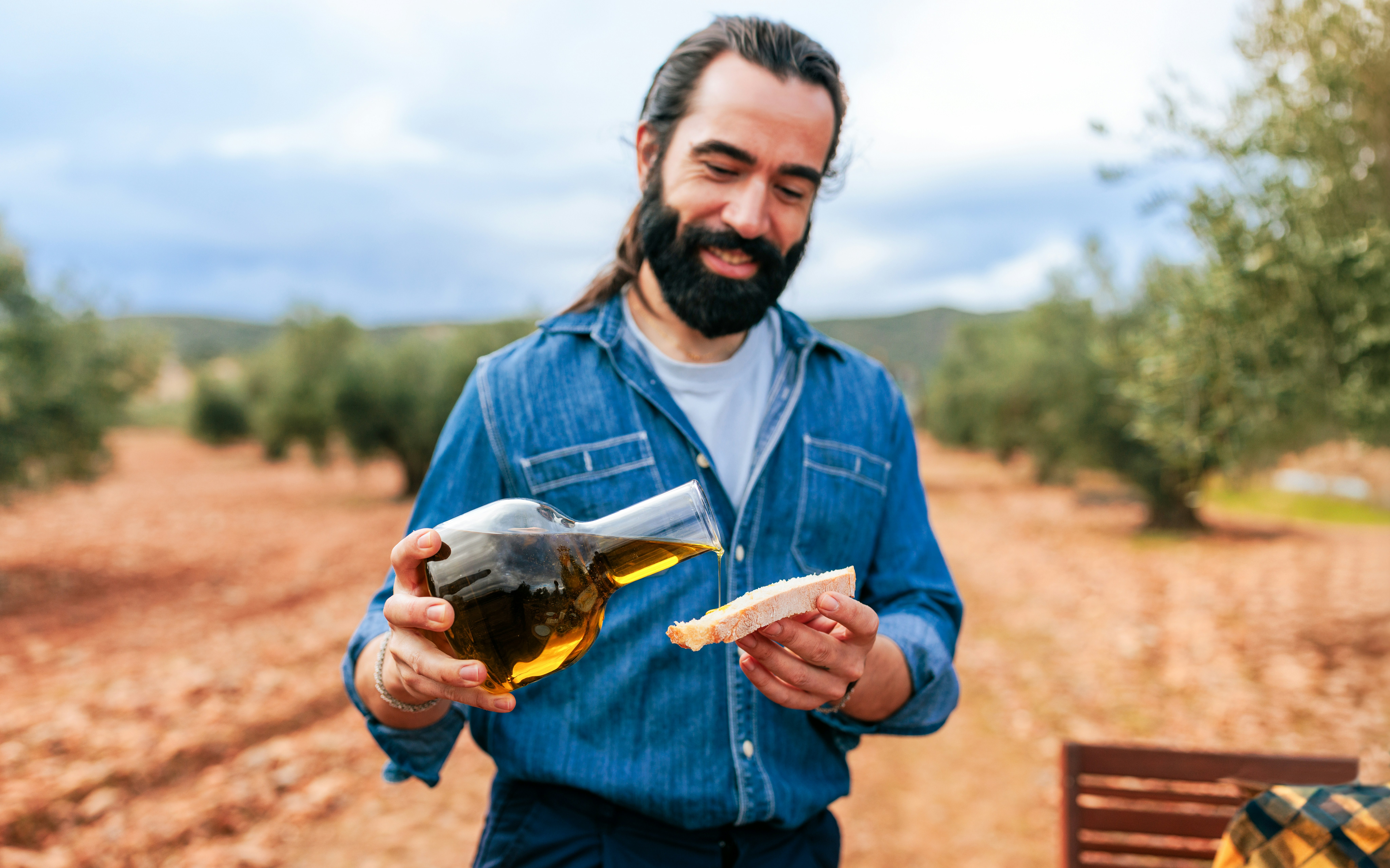 Farmer pouring olive oil on bread in an olive grove.