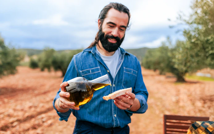 Farmer pouring olive oil on bread in an olive grove.