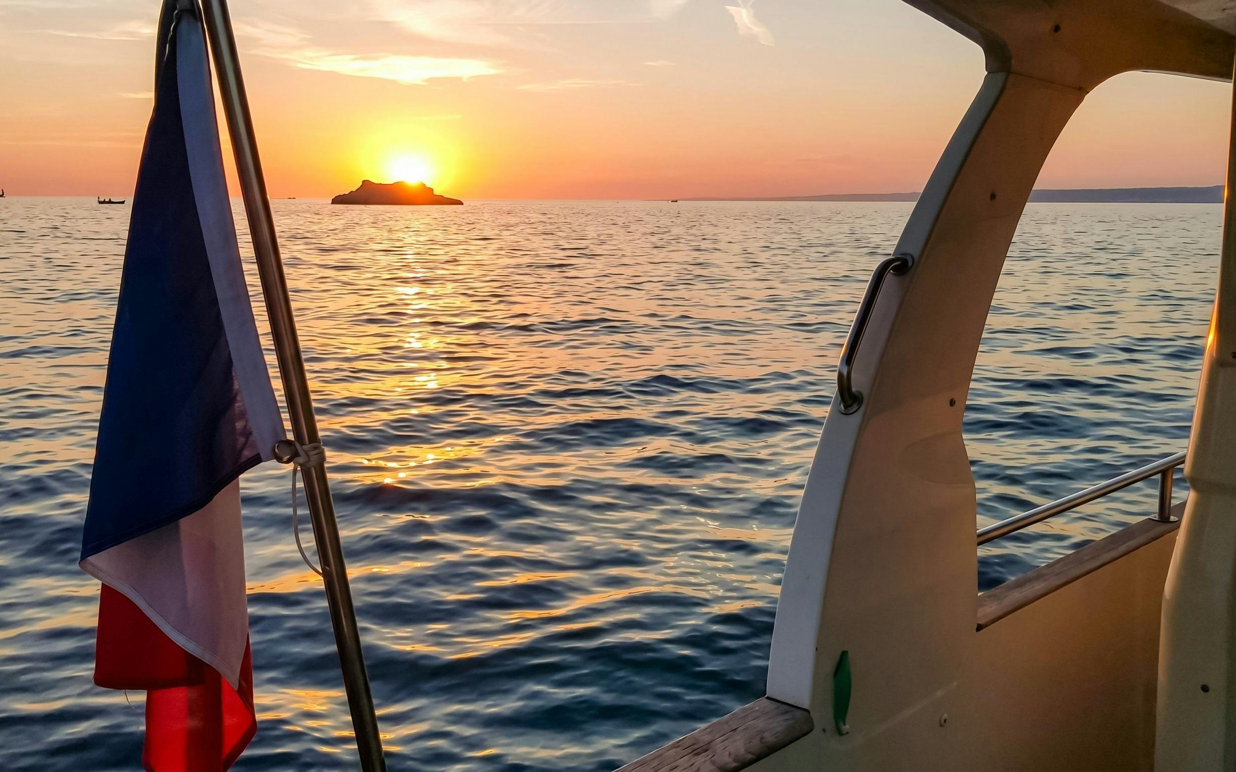 Sunset view from a boat on a Marseille dinner cruise with French flag.