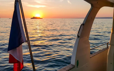 Sunset view from a boat on a Marseille dinner cruise with French flag.