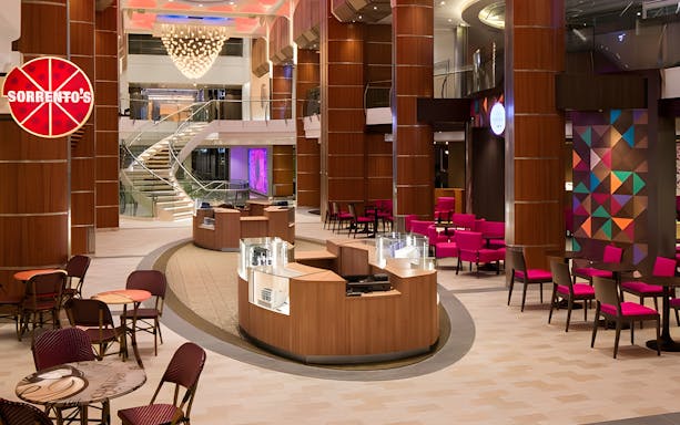 Cruise ship interior with dining area, colorful seating, and spiral staircase.