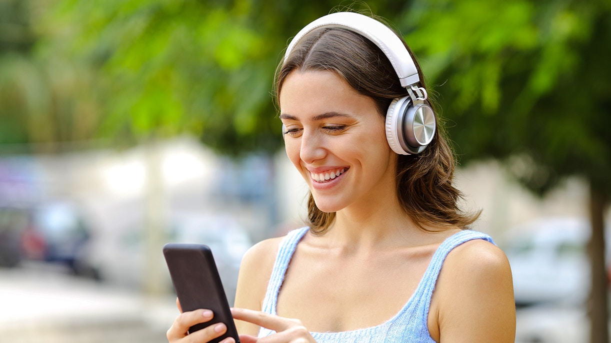 Woman using audio guide on smartphone with headphones outdoors.