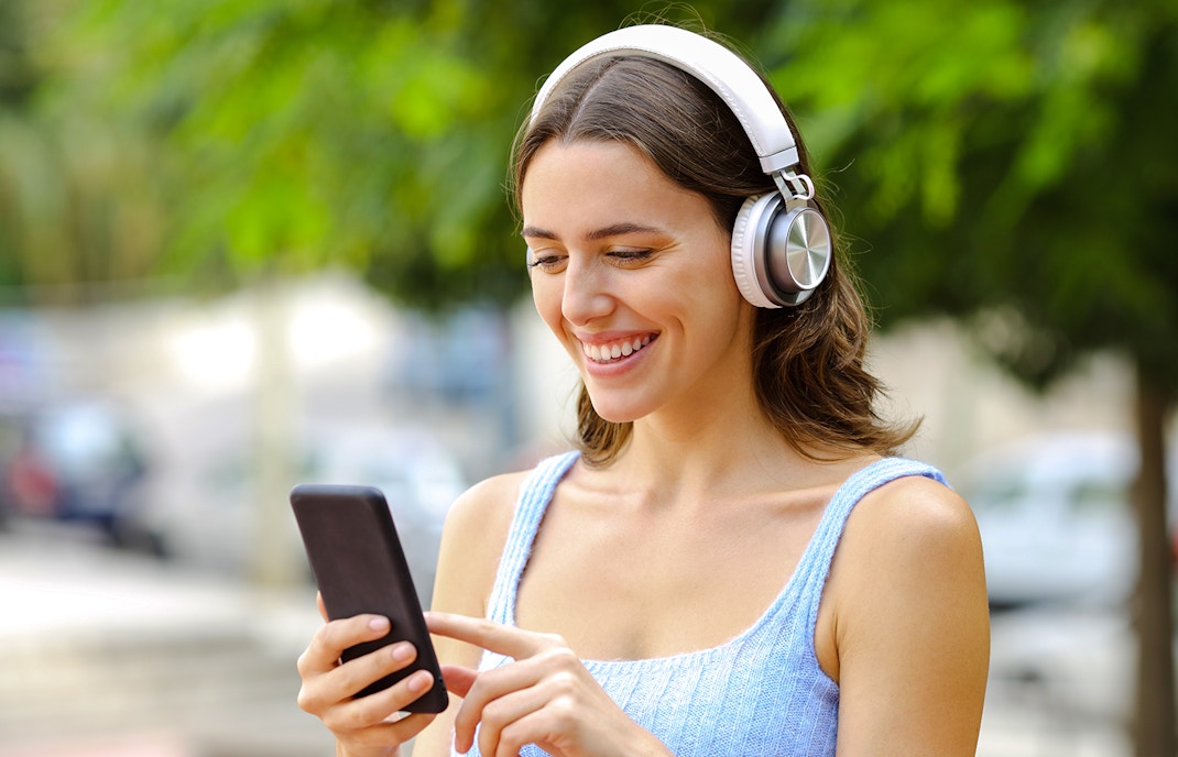 Woman using audio guide on smartphone with headphones outdoors.