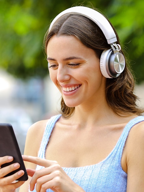 Woman using audio guide on smartphone with headphones outdoors.