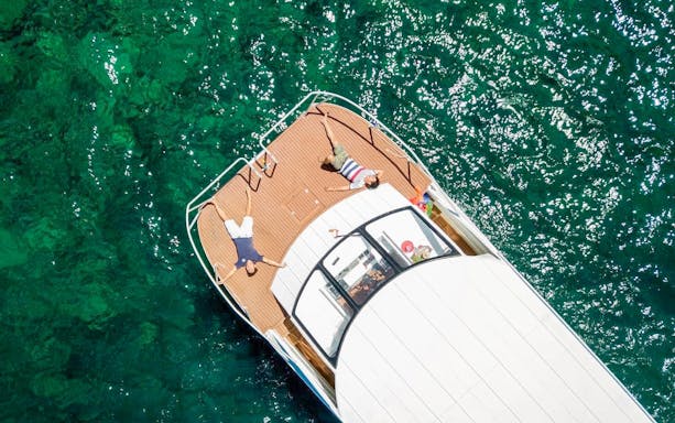 Tourists relaxing on catamaran deck over clear blue water.