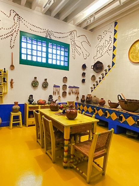 Frida Kahlo Museum kitchen with yellow furniture and traditional Mexican pottery.