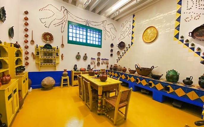 Frida Kahlo Museum kitchen with yellow furniture and traditional Mexican pottery.