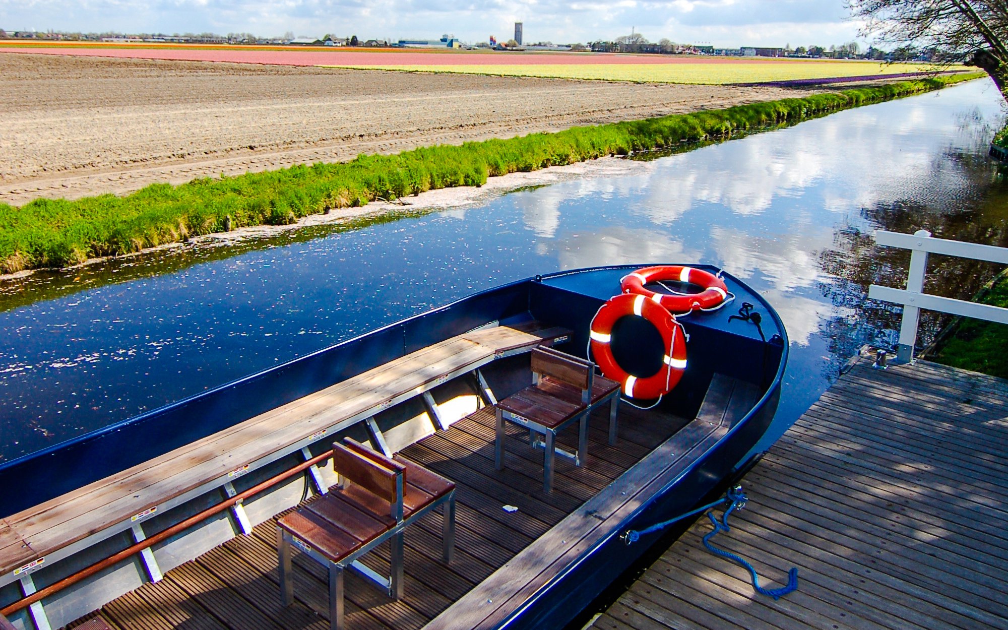 Whisper boat docked by a canal near Keukenhof with tulip fields in the background.