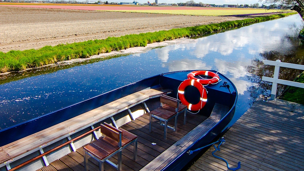 Whisper boat docked by a canal near Keukenhof with tulip fields in the background.