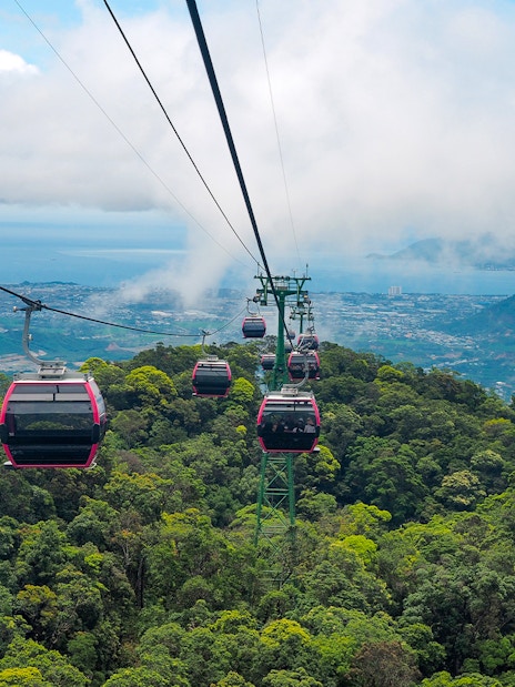 Cable cars over lush forest in Ba Na Hills, Vietnam, with distant city and ocean views.