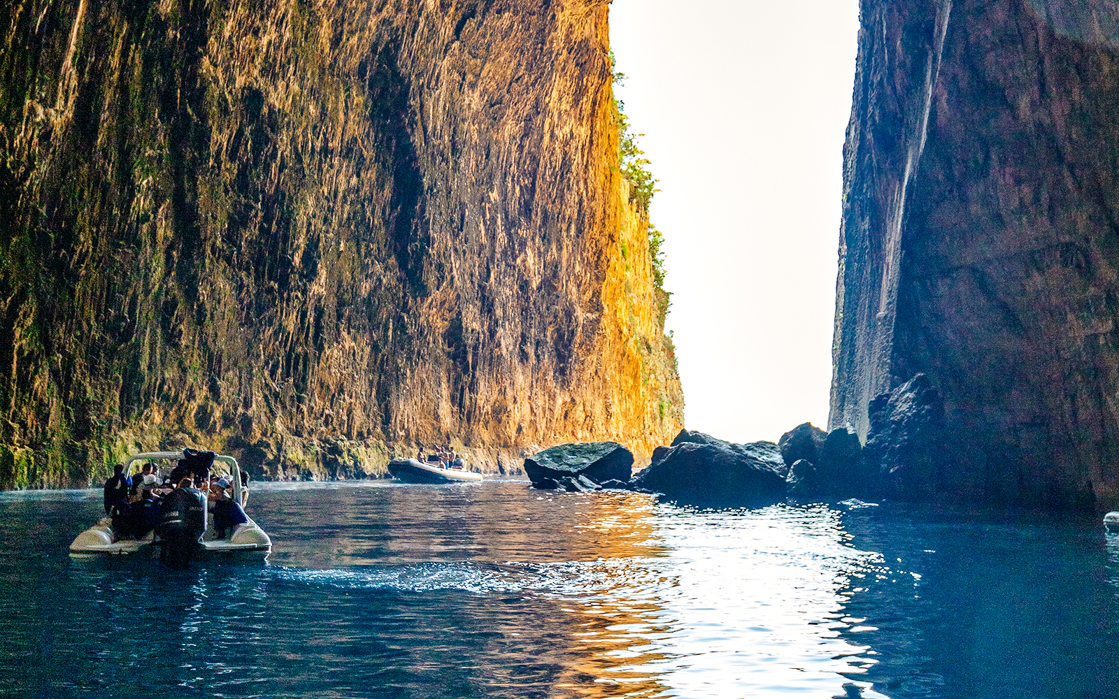 Boat entering Haxhi Ali Caves with towering rock walls and clear blue water.