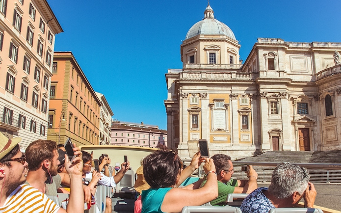 Tourists on a hop-on hop-off bus tour in Rome, photographing a historic building.