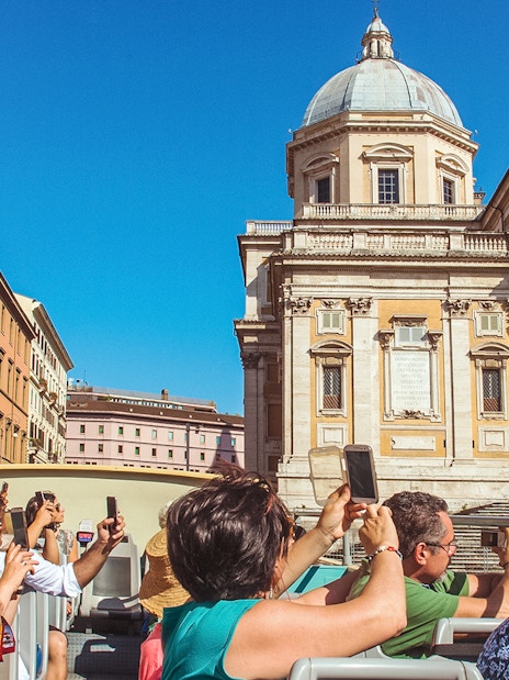 Tourists on a hop-on hop-off bus tour in Rome, photographing a historic building.