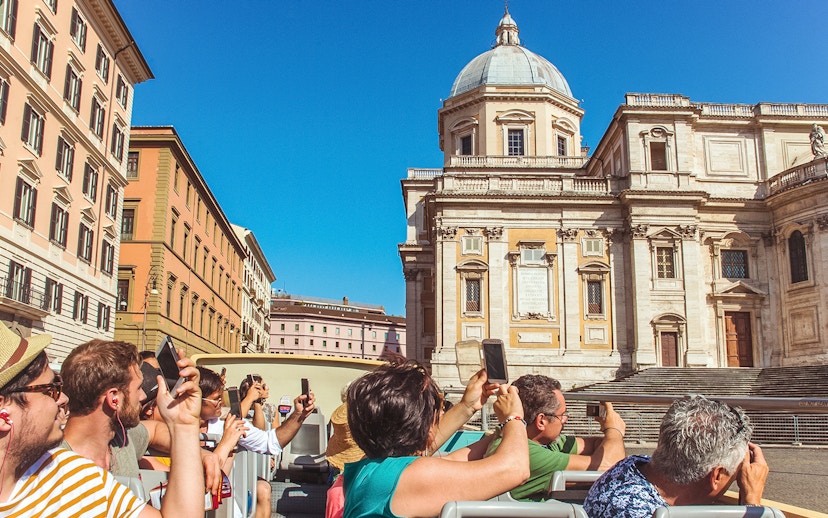 Tourists on a hop-on hop-off bus tour in Rome, photographing a historic building.