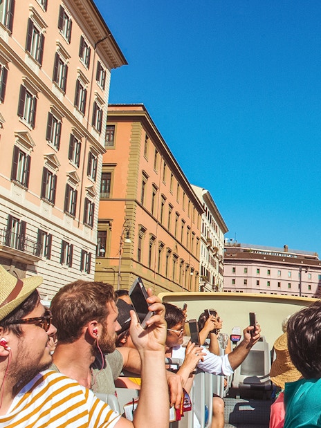 Tourists on a hop-on hop-off bus tour in Rome, photographing a historic building.