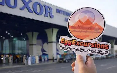 Luxor Airport entrance with a hand holding an EgyExcursions sign for private transfer service.