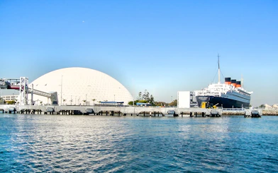 Queen Mary ship docked at Los Angeles Harbor with geodesic dome nearby.