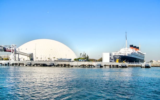 Queen Mary ship docked at Los Angeles Harbor with geodesic dome nearby.