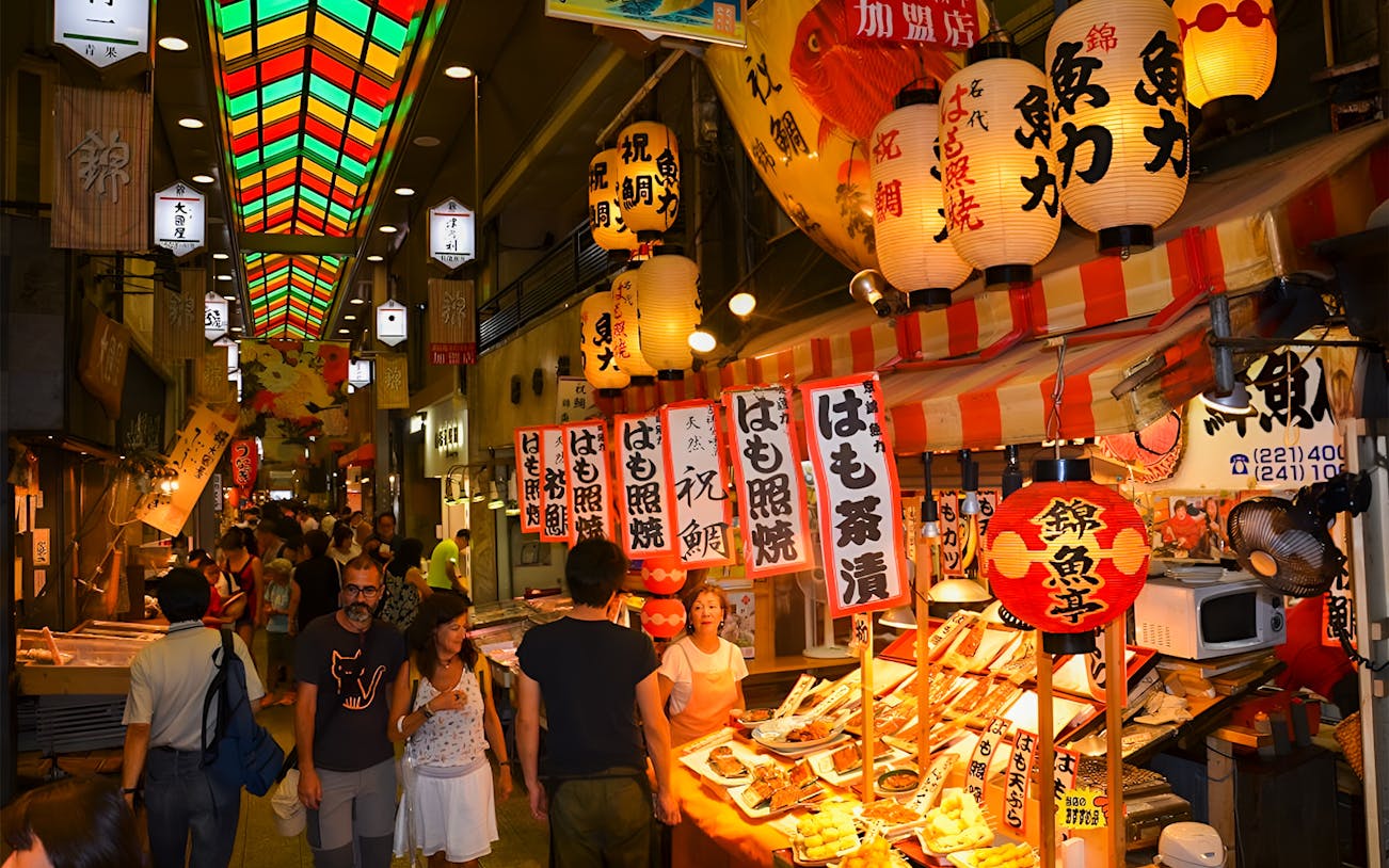 Nishiki Market in Kyoto with food stalls and colorful lanterns.