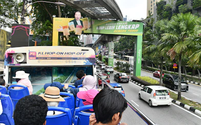 Open-top bus tour in Kuala Lumpur with passengers viewing city streets and greenery.