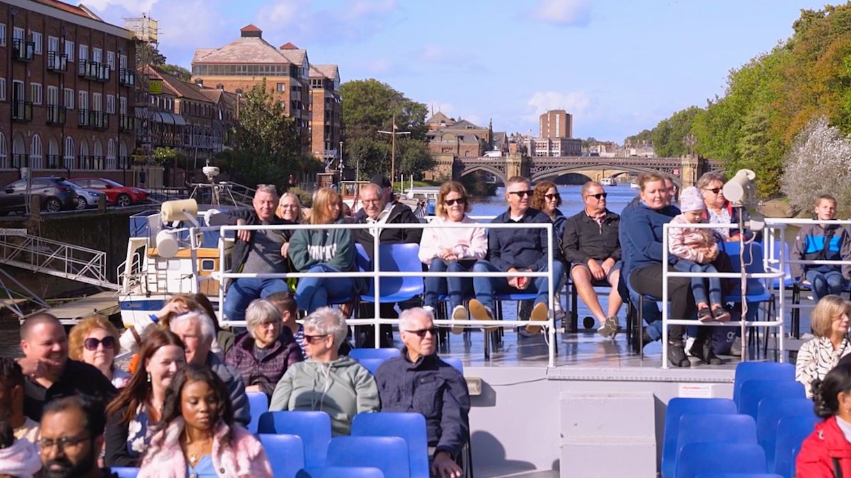 Tourists enjoying a York sightseeing cruise on a sunny day with cityscape views.