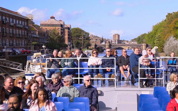 Tourists enjoying a York sightseeing cruise on a sunny day with cityscape views.