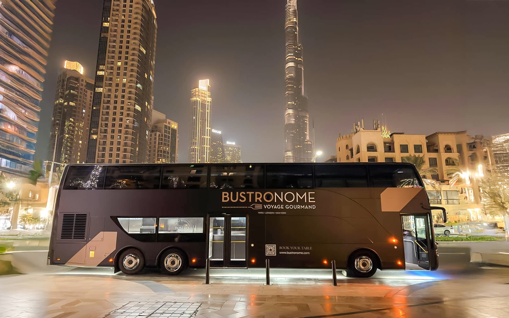 Bustronome restaurant bus parked near Burj Khalifa in Dubai at night.