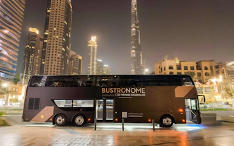 Bustronome restaurant bus parked near Burj Khalifa in Dubai at night.